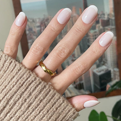 Classic French | Short | Round - Tab Press-On nails with natural base and white tips shown on hand wearing gold ring indoors