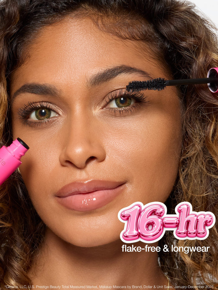 Mascara wand features twisted double fiber bristles for maximum pigment. Accompanying text highlights confidence booster brush, hourglass shape hugs lashline, and details for optimal makeup application. Background is plain.