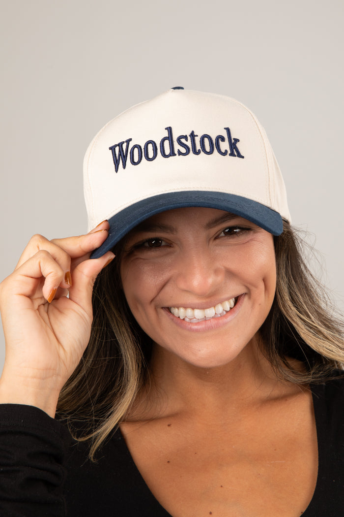 Woman wearing a white cap with 'Woodstock' text on a gray background